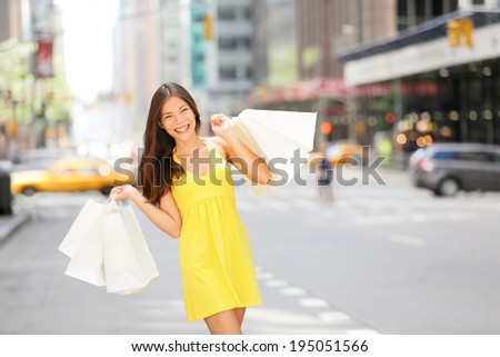 Urban shopping woman in New York City street with yellow taxi cab. Beautiful happy summer shopper holding shopping bags walking outside smiling. Multiracial Asian Caucasian model on Manhattan, USA.