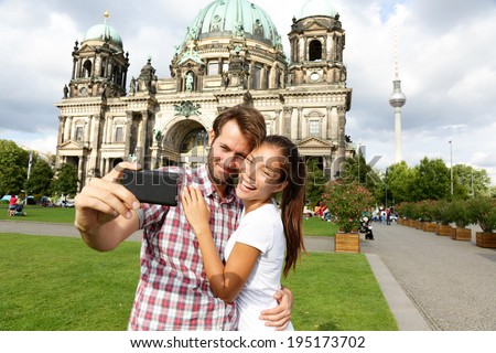 Berlin Germany travel couple selfie self portrait. Happy tourists people in front of Berlin Cathedral / Berliner Dom with Fernsehturm / Berlin TV Tower in the background. Asian woman, Caucasian man.