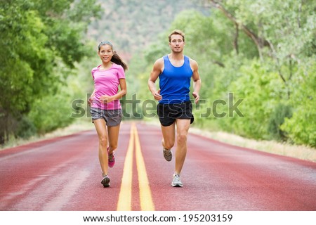 Running young multicultural couple exercising fitness outside on road in pretty nature jogging happy smiling. Asian female model and Caucasian male model training together.