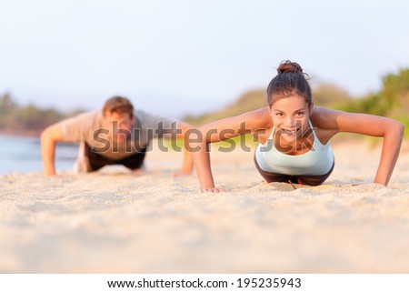 Fitness young people doing pushups on beach. Fit couple, female sport model and man training crossfit outdoors. Multiracial couple, Asian woman Caucasian man athlete in their 20s.