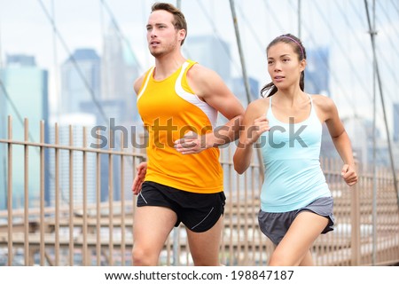 Running couple jogging training for New York marathon. Runners on run outside. Asian woman and Caucasian man runner and fitness sport models jogging on Brooklyn Bridge, New York City, USA.