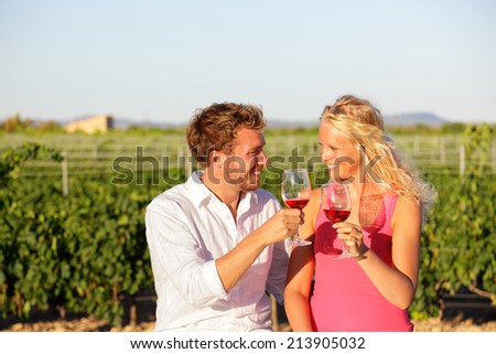 Red wine drinking couple toasting at vineyard. People drinking red or rose wine smiling happy doing toast. Romantic lovers outside. Young Caucasian man and woman.