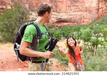 Helping hand - hiking woman getting help on hike smiling happy. Active lifestyle hiker couple traveling. Beautiful smiling mixed race Asian Caucasian female in Zion National Park, Utah, USA.