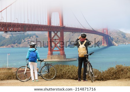 Golden gate bridge - biking couple sightseeing in San Francisco, USA. Young couple tourists on bike tour enjoying the view at the famous travel landmark in California, USA.