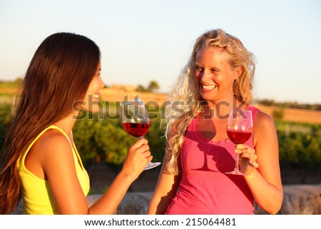 Wine drinking friends toasting drinks at vineyard. Two women cheering with a glass of rose or red wine in summer.