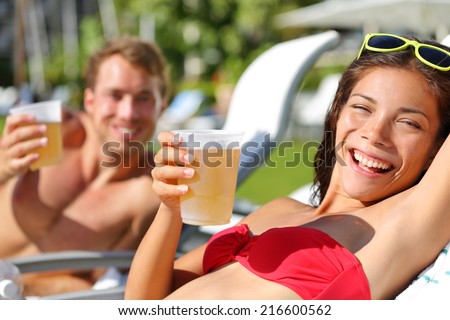 People drinking beer at relaxing at beach resort having fun enjoying spring break. Young couple relaxing drinking alcoholic drink on summer vacation holidays travel.