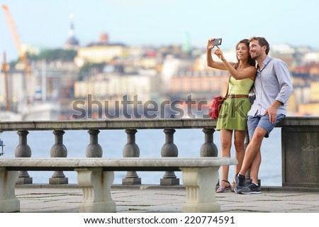 Europe travel. Romantic couple tourists in Stockholm taking selfie photo having fun enjoying skyline view and river by Stockholms City Hall, Sweden.