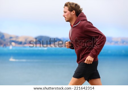 Runner athlete man running in sweatshirt hoodie in autumn fall by the water. Male runner training outdoors jogging in nature.