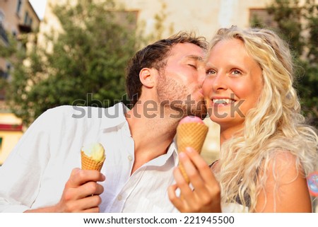 Couple eating ice cream kissing happy having fun in love enjoying summer romance in city. Happy romantic woman and man eating ice cream cone outdoors in summer on travel holidays vacation.
