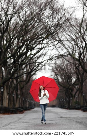 Girl with red umbrella walking in park in fall. Happy smiling multiracial Asian woman walking cheerful with red umbrella in Central Park, Manhattan, New York City, USA.