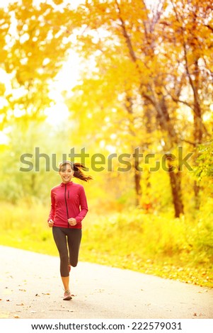 Athlete runner woman running in fall autumn forest. Female fitness girl jogging on path in amazing fall foliage landscape nature outside.