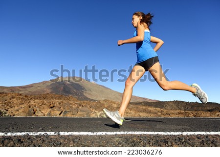 Sprinting running woman - female runner training outdoors jogging on mountain road in amazing landscape nature. Fit beautiful fitness model working out for marathon outside in summer.