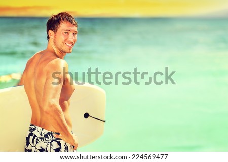 Surfer man going surfing on summer beach. Male bodyboarding surfing man good looking standing with bodyboard surfboard during vacation holidays getaway. Caucasian water sport model in his 20s.