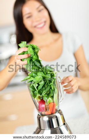 Green smoothie woman making vegetable smoothies with blender. Healthy eating lifestyle concept portrait of beautiful young woman preparing drink with spinach, carrots, celery etc at home in kitchen.