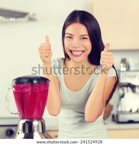 Smoothie woman making fruit and berry smoothies giving thumbs up happy by blender. Healthy eating lifestyle concept portrait of beautiful young woman preparing drink blending strawberries, raspberries