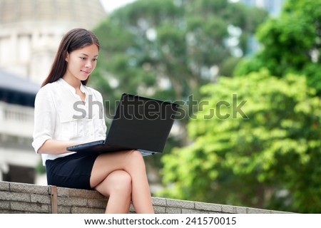 Business woman with computer laptop working outside looking at screen in business district, Central, Hong Kong. Young female professional businesswoman sitting outdoors. Asian Chinese Caucasian woman.