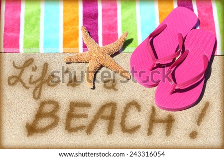 Beach travel fun sign. LIFE IS A BEACH written in sand with water next to beach towel, summer sandals and starfish. Summer and sun vacation holidays concept background.