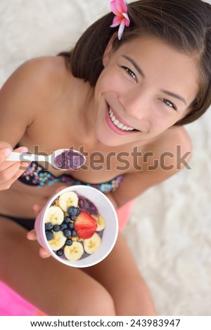Acai bowl - woman eating healthy food on beach. Girl enjoy acai bowls made from acai berries and fruits outdoors on beach for breakfast. Girl on Hawaii eating local Hawaiian dish.