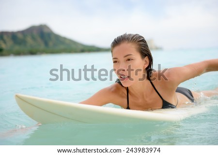 Surfing surfer girl paddle for surf on surfboard. Female bikini woman living healthy active water sports lifestyle on Hawaiian beach. Asian Caucasian model on Waikiki Beach, Oahu, Hawaii.