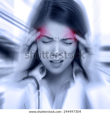 Young woman with a pounding headache or migraine standing clutching her temples with an expression of pain, monochrome image with selective red color to temples and blur effect around her face