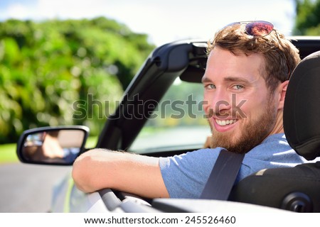 Car driver - young man wearing safety belt driving convertible on road trip in summer. Caucasian male looking at camera.