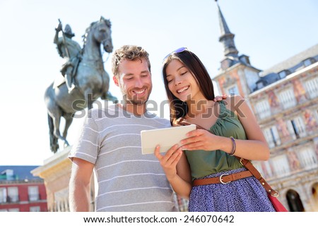 Madrid tourists using tablet travel app guidebook ebook on Plaza Mayor by statue of King Philip III. Tourist couple sightseeing visiting tourism landmarks and attractions in Spain. Young woman and man