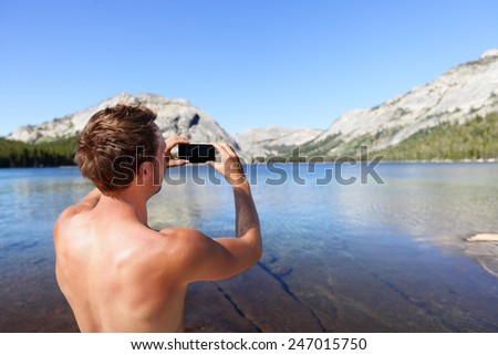 Mobile photography - man taking picture with phone. Young adult photographer holding smartphone taking pictures of nature landscape. Lake in Yosemite National Park, California, USA.