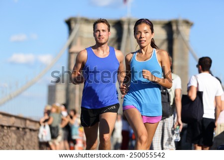 City running couple jogging outside. Runners training outdoors working out in Brooklyn with Manhattan, New York City in the background. Fit multiracial fitness couple, Asian woman, Caucasian man.