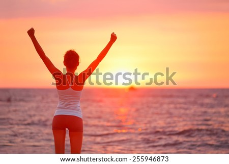 Happy cheering celebrating success woman at beautiful beach sunset. Fitness girl enjoying view with arms raised up towards the sky. Happy free freedom sport concept image outdoors.