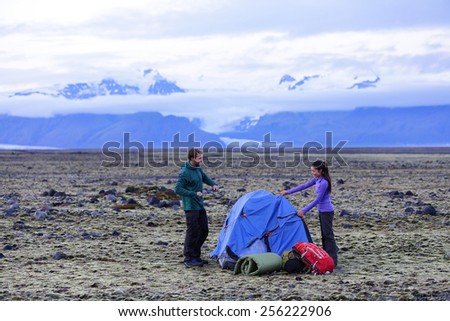 Camping couple pitching tent after hiking. Friends putting up tent for the night after hike with gear and backpacks. Active lifestyle image with Caucasian man and Asian woman.