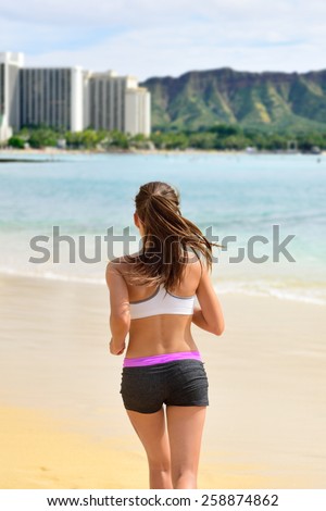 Active fit female sport runner jogging on beach. Woman jogger from behind working out her cardio by running on sunny Waikiki beach, Honolulu city, Oahu island, Hawaii, USA.