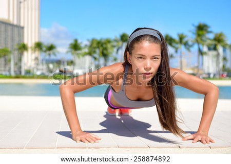 Push-ups fitness woman doing pushups toning arms outside on beachwalk. Fit female sport model girl training crossfit exercise outdoors. Mixed race Asian Caucasian sport athlete in her 20s.