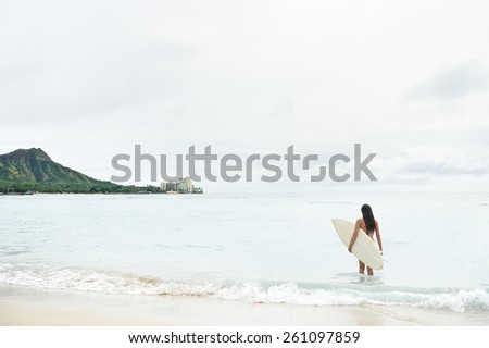 Surfer girl going surfing on Waikiki Beach, Oahu, Hawaii. Female bikini woman heading for waves with surfboard having fun living healthy active lifestyle on Hawaiian beach. Water sports with model.