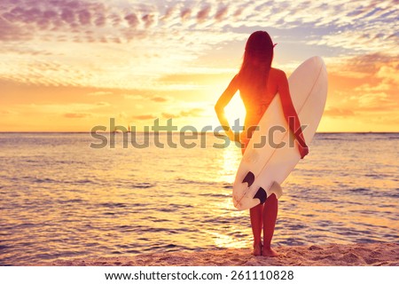 Surfer girl surfing looking at ocean beach sunset. Beautiful sexy female bikini woman looking at water with standing with surfboard having fun living healthy active lifestyle. Water sports with model.