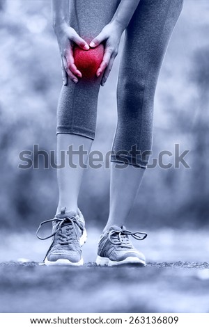 Knee injury - runner with sprained leg joint pain. Closeup of female athlete's leg with red circle showing pain. Woman holding with hands around hurting knee in summer nature background.