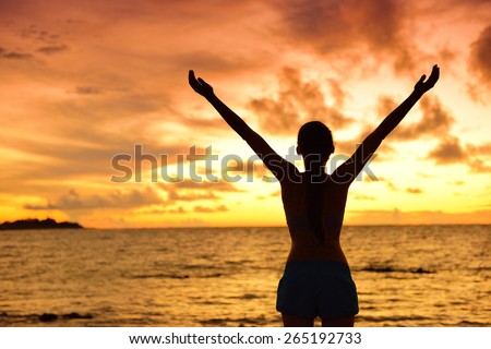 Freedom woman silhouette living healthy lifestyle a happy carefree and free life. Portrait from the back of an unrecognizable female adult at beach holidays in sunset with arms raised up in the sky.