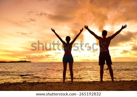 Freedom people living a free, happy, carefree life at beach. Silhouettes of a couple at sunset arms raised up showing happiness and a healthy lifestyle against a colorful sky of clouds background.