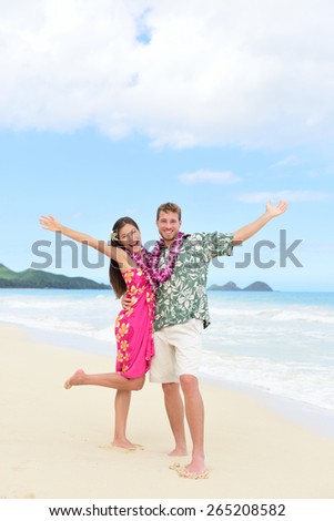 Happy Hawaii vacation couple having fun on beach holidays in Hawaii standing on perfect white sand with arms up in joy and happiness. People ready for summer vacations showing freedom and success.