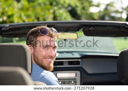 Car driver man driving convertible on a road trip. Portrait of a young Caucasian male adult looking at camera in his new or rental automobile happy to travel on holiday for summer vacations.
