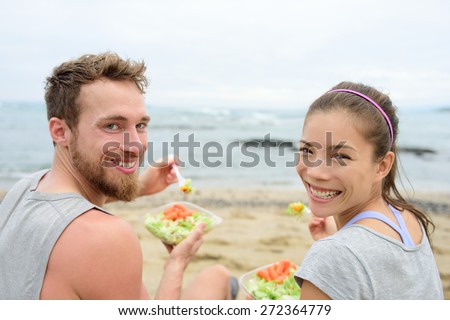 Vegan friends eating vegetarian salad meal during lunch break on beach happy looking at camera. Multiethnic group of young people, Caucasian man, Asian chinese mixed race woman in their 20s.