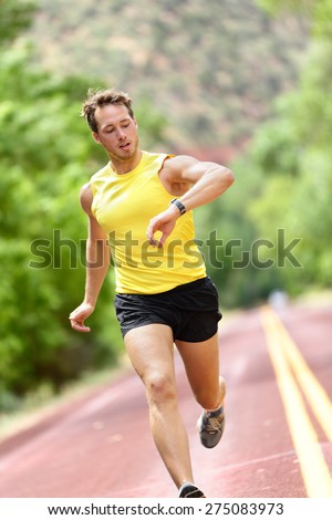 Runner looking at heart rate monitor smart watch while running. Man jogging outside looking at his sports smartwatch during workout training for marathon run. Fit male fitness model in his 20s.