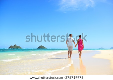 Beach honeymoon couple holding hands walking on white sand beach. Newlyweds happy in love relaxing on summer holidays on Lanikai beach, Oahu, Hawaii, USA with Mokulua Islands. Travel vacation concept.