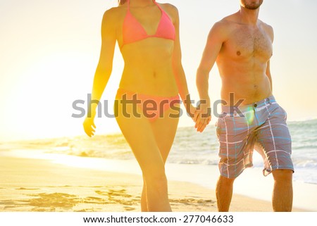 Summer beach couple romantic holding hands at sunset walking in love on honeymoon travel vacation holidays. Unrecognizable woman and man in happy romance wearing bikini and casual beachwear shorts.
