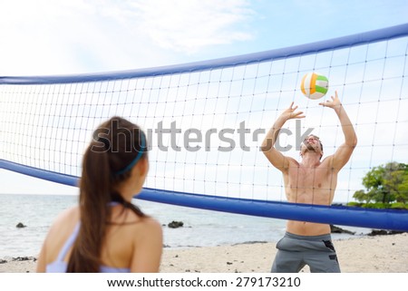 People playing beach volleyball having fun in sporty active lifestyle. Man hitting volley ball in game in summer. Woman and man fitness model living healthy lifestyle doing sport on beach.