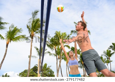 Friends playing beach volleyball sport in summer. Woman volley the ball to man jumping to smash. People having fun recreational volley ball game living healthy active sport lifestyle.