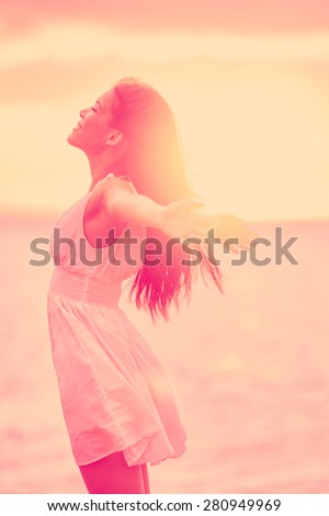 Freedom - Free happy serene woman enjoying sunset. Beautiful woman in dress embracing the golden sunshine glow of sunset with arms outspread and face raised in sky enjoying peace, serenity in nature