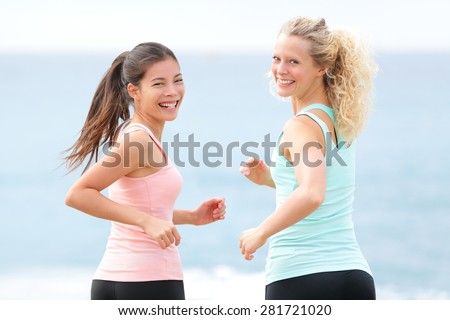 Women running exercising. Two young fit female friends runners smiling jogging on summer beach enjoying healthy lifestyle. Beautiful fitness models turning towards camera in summer.