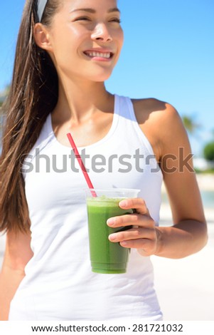 Green smoothie. Woman holding green vegetable detox juice outside in summer sun. Healthy lifestyle with beautiful mixed race Asian Caucasian female model taking a cleanse diet.