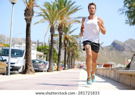 Fit male runner running outside on boardwalk. Young man model training fitness jogging on Mallorca beach city outdoors in summer sun. Palms in background. Healthy lifestyle.