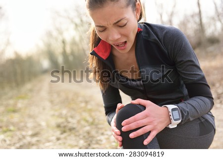 Sport and fitness injury - Female runner with hurting knee. Running woman screaming in pain during run wearing a smartwatch. Painful joint during workout.